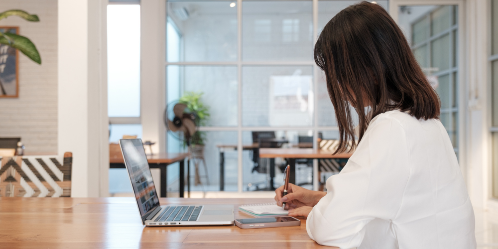Une jeune femme participe à un séminaire en ligne et prend des notes.