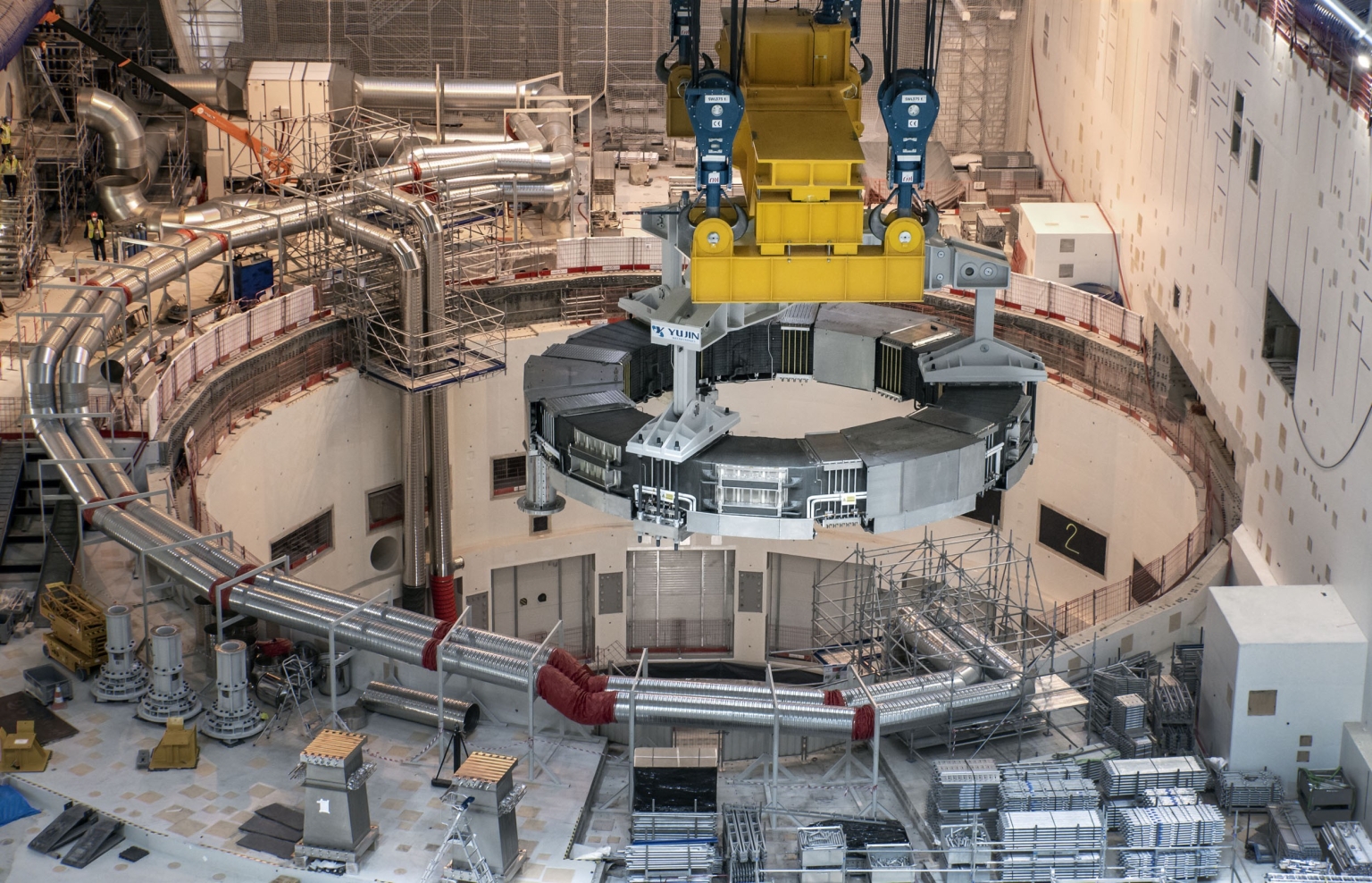 La bobine de champ poloïdal n°6 est abaissée dans la fosse du tokamak à l’aide d’un pont roulant bipoutre.
